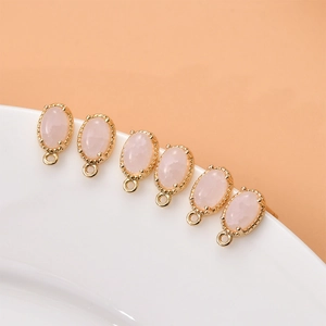 Close-up of six pink gemstone oval pendants with gold plating and hanging loops for DIY jewelry