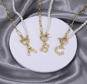 Detailed view of OT buckle pearl and gold paperclip necklace with initial pendants