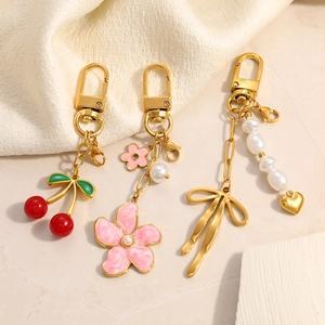 Gold stainless steel keychains with cherry, flower, pearl, and bow charms on a white textile