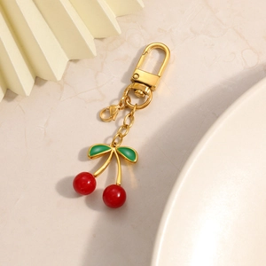 Detail of a cherry-shaped keychain with red beads and green leaves on gold plating