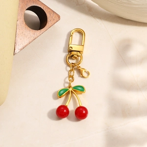 Detail of red cherry pendant keychain with gold chain and green enamel leaves