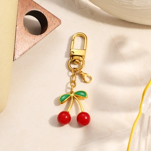 Detail of cherry keychain with red beads and green leaves on stone surface