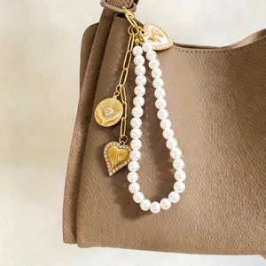 French vintage pearl bag charm with gold heart pendants on a textured leather handbag