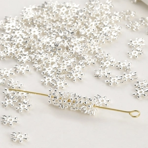 Macro shot of silver snowflake spacer beads on a gold metal needle for DIY jewelry making