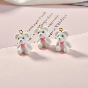 Detailed view of three white flocked teddy bear charms with pink bows for DIY jewelry making