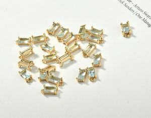 Macro view of rectangular light blue crystal charms with 18k gold plated claw settings