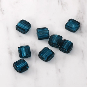 Flat lay of square deep blue glass beads with silver leaf textures on marble background