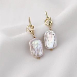 Baroque pearl drop earrings with elegant golden knot studs on white silk background