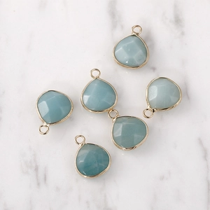 Close-up of faceted light blue water drop pendants with gold plated edges on marble