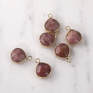 Macro detail of six pink crystal teardrop pendants with gold plated edges on marble