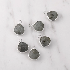 Detail of 6 teardrop labradorite stone pendants with silver metal edges on marble background