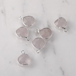 Macro view of six pink crystal teardrop charms with silver metal borders on marble
