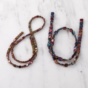 Rainbow hematite square beads with metallic luster on white marble surface