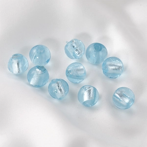 Macro shot of 10 light blue handmade glass beads with silver foil interior on silk
