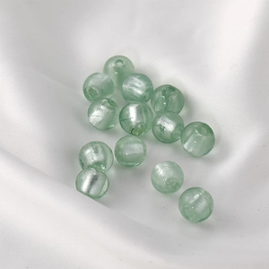 Close-up of light green translucent glass beads on white satin for jewelry making