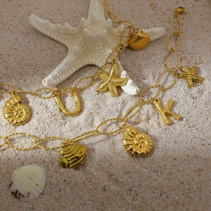 Detail of 18K gold plated anklet with starfish and shell charms on sandy beach background