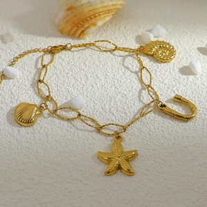 Detailed close-up of 18K gold plated anklet with starfish and seashell charms on sand