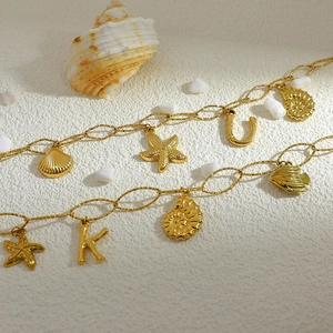 Detail of 18K gold plated anklet featuring starfish, seashell, and letter charms on sand