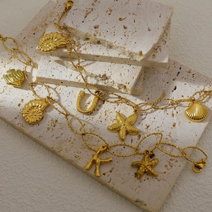 18K gold plated stainless steel anklet with ocean charms and letters on travertine