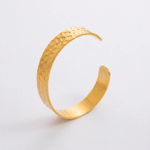 Dettaglio della texture martellata dorata e del design irregolare del bracciale aperto a C