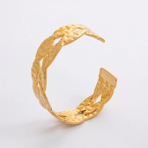 Dettaglio del bracciale rigido dorato martellato con design a trama aperta e lucido