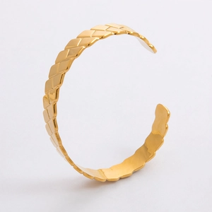 Dettaglio del bracciale rigido dorato aperto con texture martellata e bordi irregolari