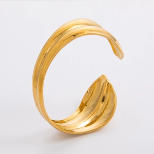 Dettaglio della trama a foglia martellata su un ampio bracciale rigido dorato a forma di C