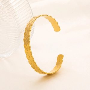 Macro di bracciale rigido dorato con trama a griglia martellata su tessuto di seta