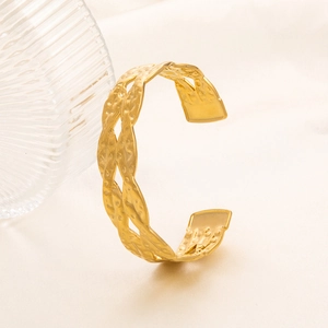 Dettaglio della trama martellata dorata sull'ampio bracciale rigido a C con design intrecciato
