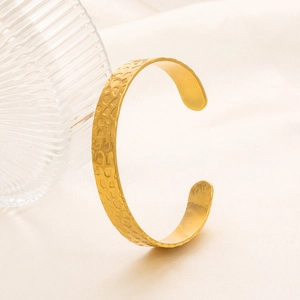 Dettaglio del bracciale aperto a C dorato con trama martellata su tessuto morbido