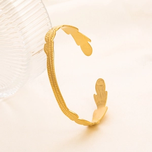 Bracciale rigido aperto dorato con foglie e trama martellata su sfondo neutro