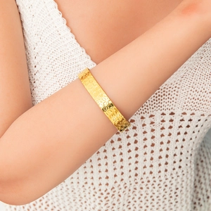 Dettaglio macro di un ampio bracciale rigido dorato con superficie in metallo martellato