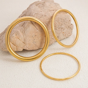 Vista detallada de tres brazaletes de acero inoxidable bañados en oro 18K sobre piedra