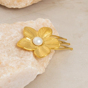 Golden flower hair clip with pearl center and textured petals on stone display