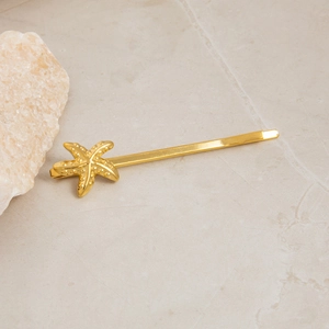 Close-up of golden starfish hair clip on marble surface with natural stone detail