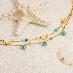 Detail der doppelreihigen Gold-Fußkette mit Kleeblatt und Türkisperlen auf hellem Sand