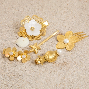 Golden starfish and shell hair clips with pearls on a beach sand background