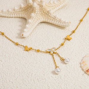 Detail der goldenen Schmetterlings-Fußkette mit Perlen auf weißem Sand mit Meeresmotiven