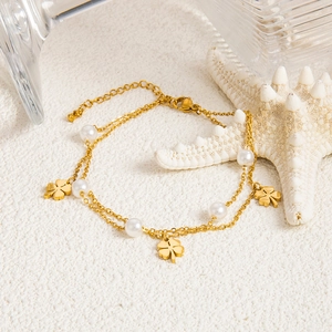 Elegantes goldene Doppel-Fußkettchen mit Perlen und Kleeblatt-Anhängern auf weißem Sand