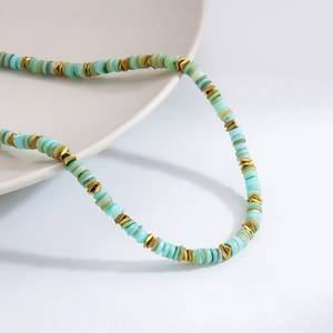 Gros plan d'un collier bohème avec perles de coquillage bleu clair et entretoises en or 18K