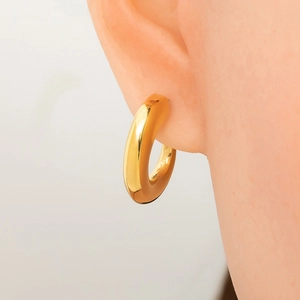 Close-up of chunky gold hoop earrings with mirror polish finish on a female ear