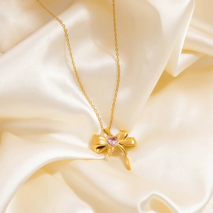 Detailansicht der goldenen Schleife mit rosa Herzstein auf cremefarbenem Seidenhintergrund