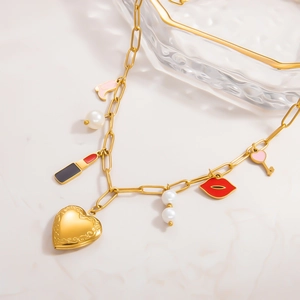 Collar de oro 18k con dijes de corazón, lápiz labial y perlas sobre fondo de mármol