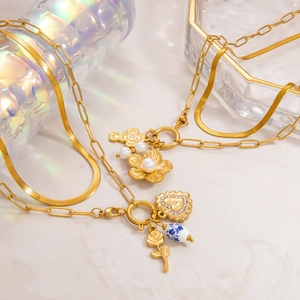 Détail d'un collier doré 18 carats avec fleur en perle, croix et perle en céramique