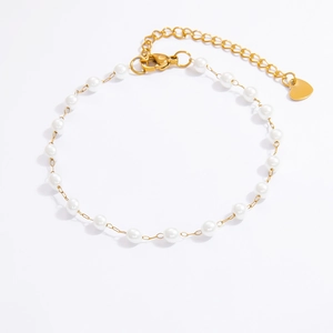 Détail du bracelet doré avec perles blanches et pendentif en forme de cœur poli