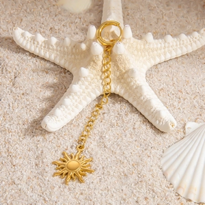 Detail of golden stainless steel earring with sun pendant on white sand with seashells