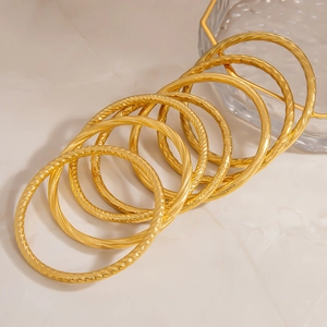 Close-up of stacked 18K gold plated stainless steel bangles with engraved spiral patterns