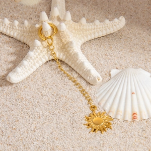 Close-up of golden stainless steel sun pendant on white starfish and sand beach background