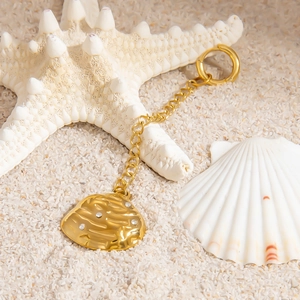 Detail of 18K gold starfish shell pendant with white diamonds on white beach sand