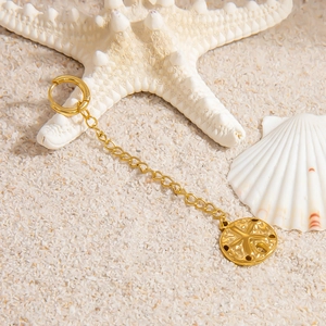 Macro view of gold stainless steel huggie hoop earrings with shell pendant on sand